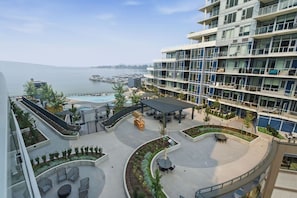 A multi-story hotel with a pool area, outdoor seating, and a view of the sea. - Beachfront Living | 2BR | Pool & Fitness Centre (Kelowna)