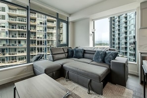 Ein modernes Wohnzimmer mit einer Eckcouch, großen Fenstern und Blick auf einen Wolkenkratzer.