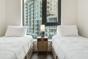Une chambre d’hôtel avec deux lits, une table de chevet, une lampe et une fenêtre donnant sur un immeuble de grande hauteur.