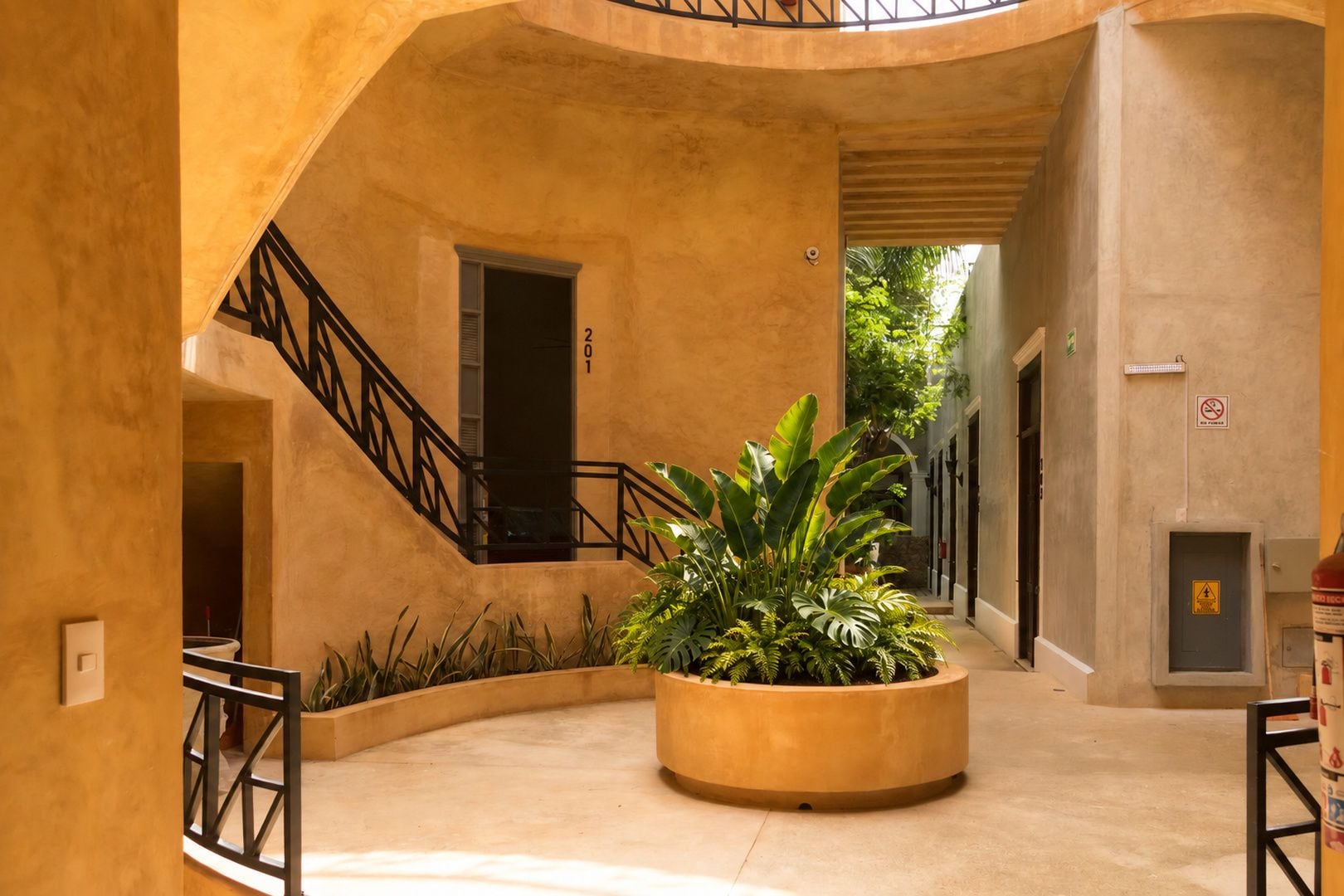 Un patio circular con un macetero central, una escalera y una puerta marcada con el número 201.