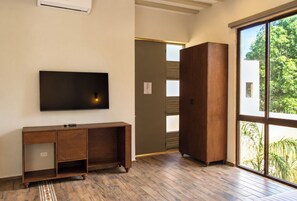 A room with a large flat-screen TV mounted on the wall, a wooden cabinet, and a sliding glass door leading to an outdoor area with greenery. - Hotel Casa Nuuma (Merida)