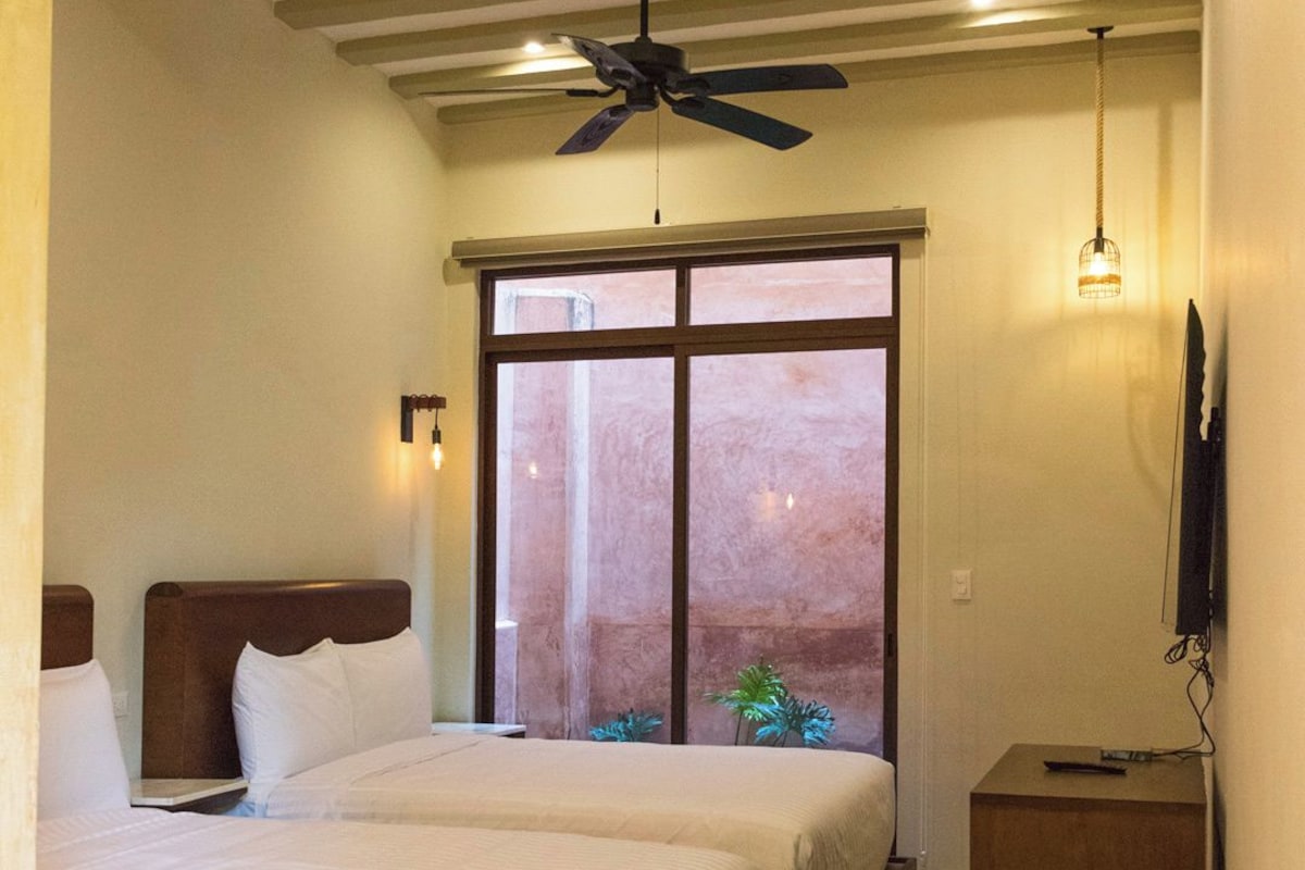 A hotel room with a large bed, a ceiling fan, a window with a view, and a bedside table.
