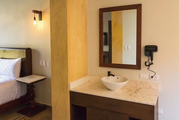 Una habitación de hotel con cama, mesita de noche, baño con lavamanos, espejo y teléfono.