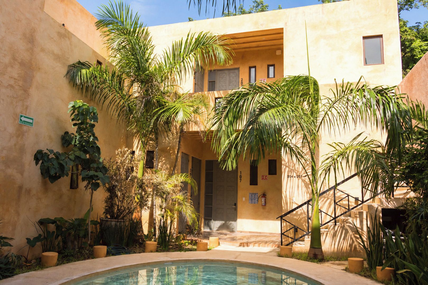 Un área de piscina con un edificio, palmeras y una escalera.