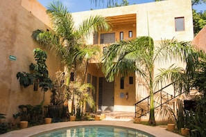 A pool area with a building, palm trees, and a staircase. - Hotel Casa Nuuma (Merida)