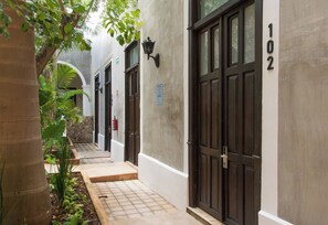A narrow pathway leading to a building with numbered doors, a fire extinguisher, and a wall-mounted light fixture. - Hotel Casa Nuuma (Merida)