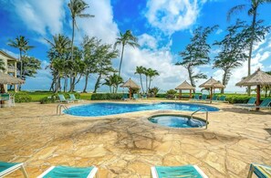 Un espace piscine doté de chaises longues, d’un jacuzzi et de palmiers.