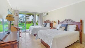 Ett hotellrum med två sängar, ett skrivbord och utsikt över en trädgård.