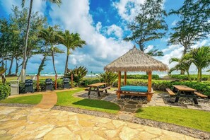 Une terrasse au bord de la plage, agrémentée d’un gazebo à toit de chaume, de tables de pique-nique et de barbecues.
