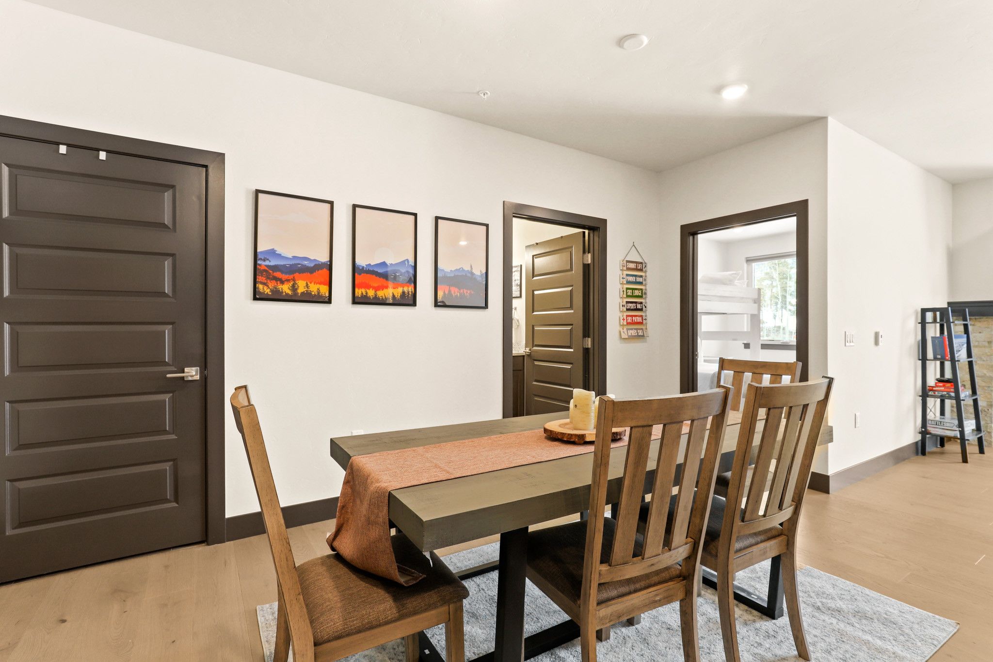 A dining area with a table, chairs, and a rug. There are framed pictures on the wall and a sign with amenities listed.