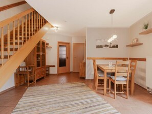 A wooden staircase leading to a dining area with a table and chairs, a patterned rug, and a wall-mounted light fixture. - 8/t5 Holiday Home Park \"freesenbruch\" (Zingst)