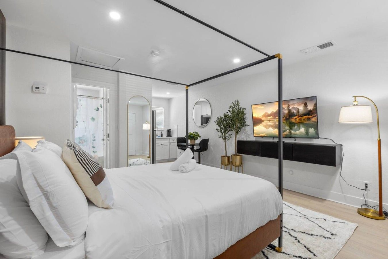 Een moderne slaapkamer met een hemelbed, een flatscreen-tv, een bureau met stoel en een grote spiegel.