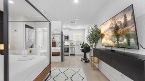 A modern hotel room with a bed, a bathroom, a kitchenette, and a large TV on the wall. - South Tampa Stay | Free Parking (Tampa)