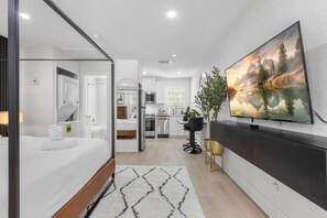 Ein modernes Hotelzimmer mit Bett, Badezimmer, Küchenzeile und einem großen Fernseher an der Wand.