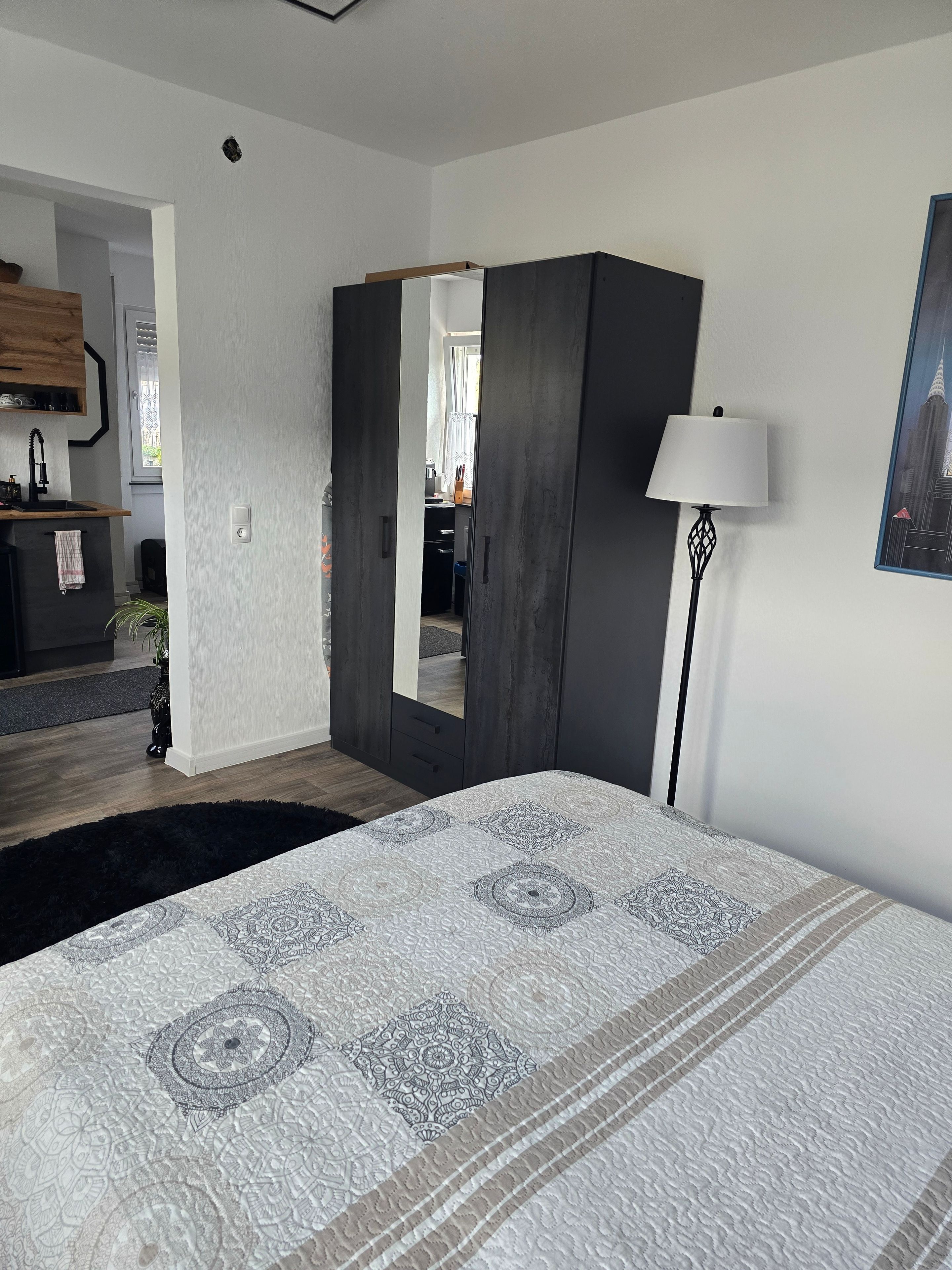 A bedroom with a bed, a wardrobe, a mirror, a lamp, and a painting on the wall.
