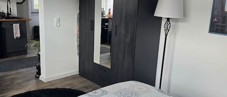 A bedroom with a bed, a wardrobe, a mirror, a lamp, and a painting on the wall.