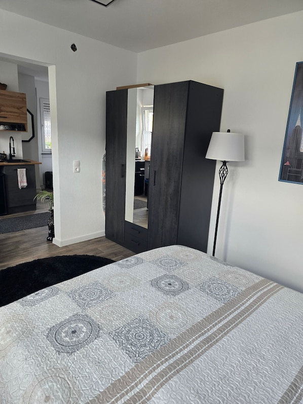 A bedroom with a bed, a wardrobe, a mirror, a lamp, and a painting on the wall.