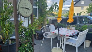 Un patio con mesa y sillas, rodeado de macetas con plantas y un reloj.