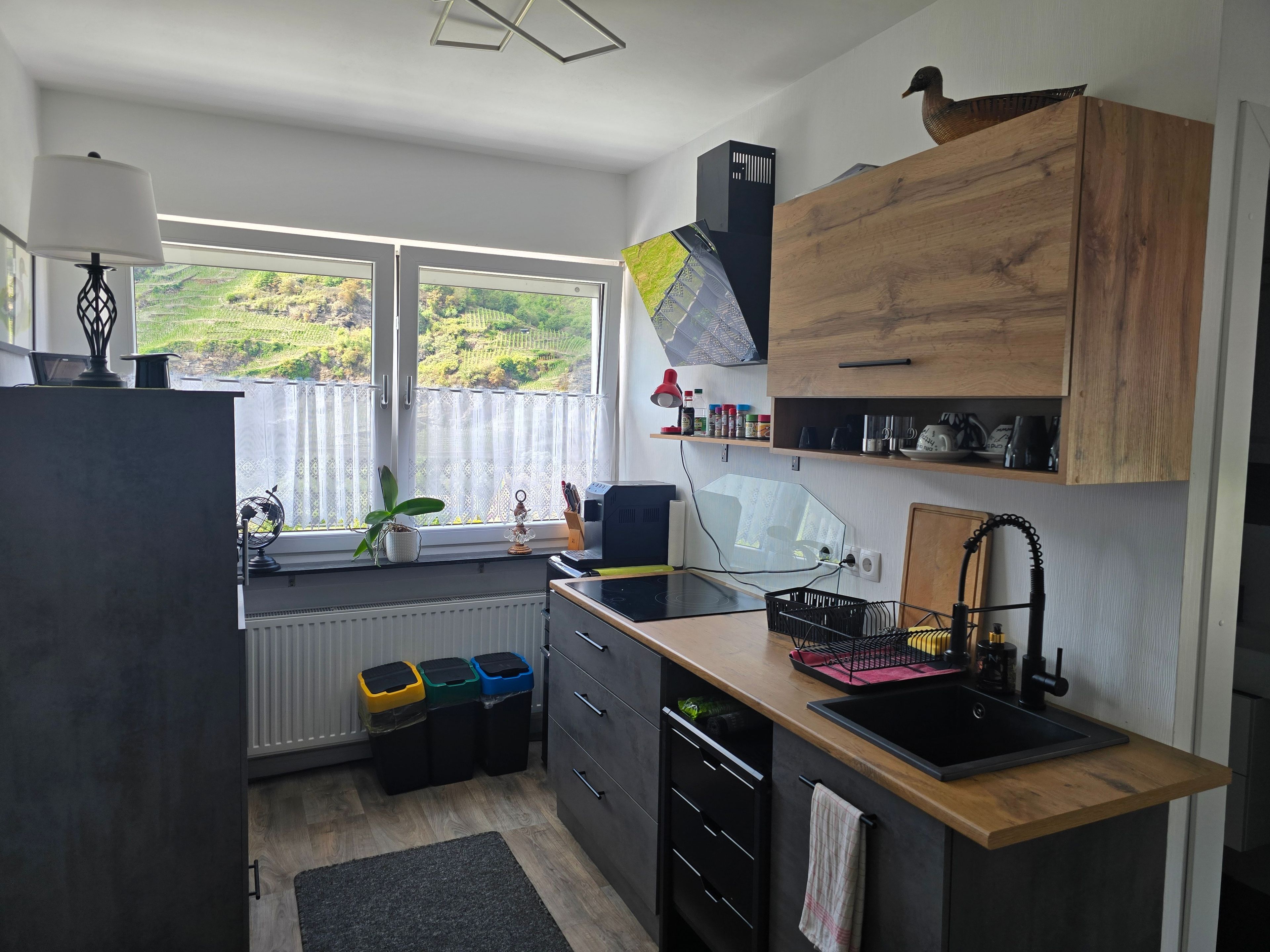 Cozinha moderna com uma janela ampla, armários de madeira, uma pia e bancada com diversos objetos.