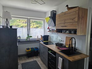 Een moderne keuken met een groot raam, houten kastjes, een spoelbak en een aanrecht met diverse spullen.