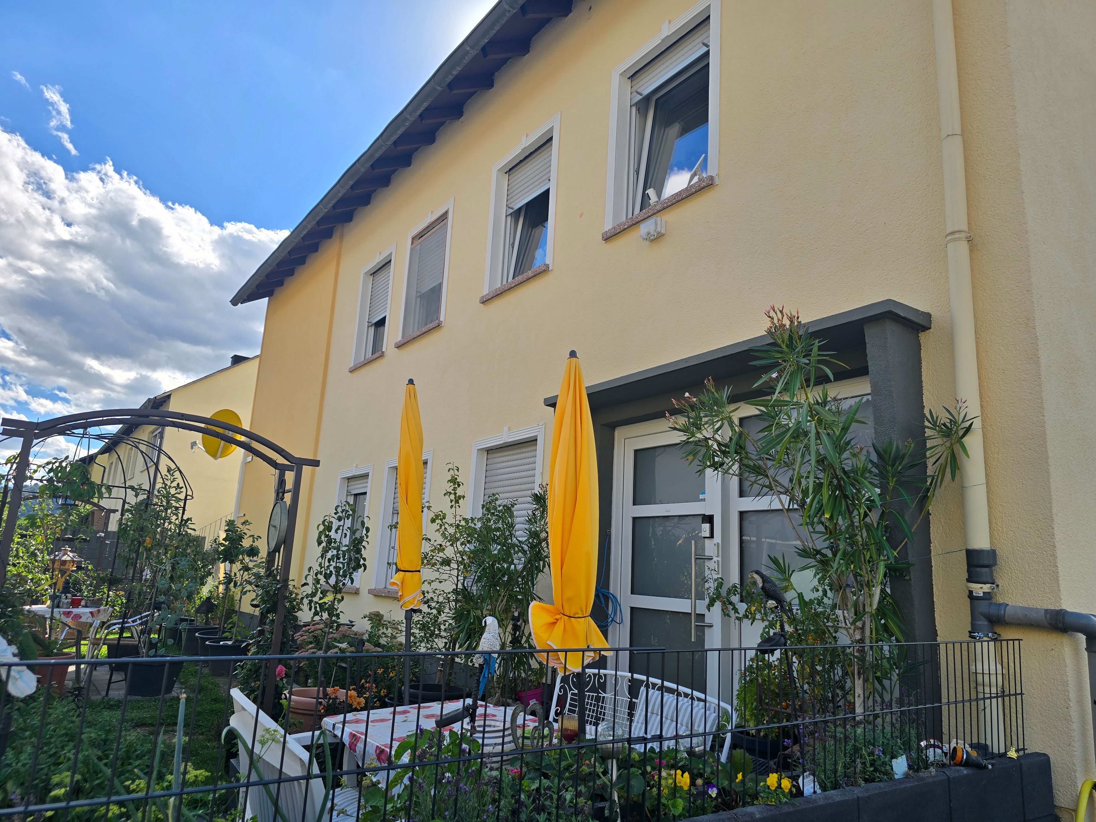 A yellow building with multiple windows, outdoor umbrellas, and a fenced garden area.