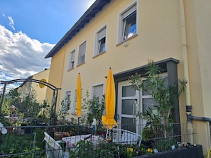 A yellow building with multiple windows, outdoor umbrellas, and a fenced garden area.