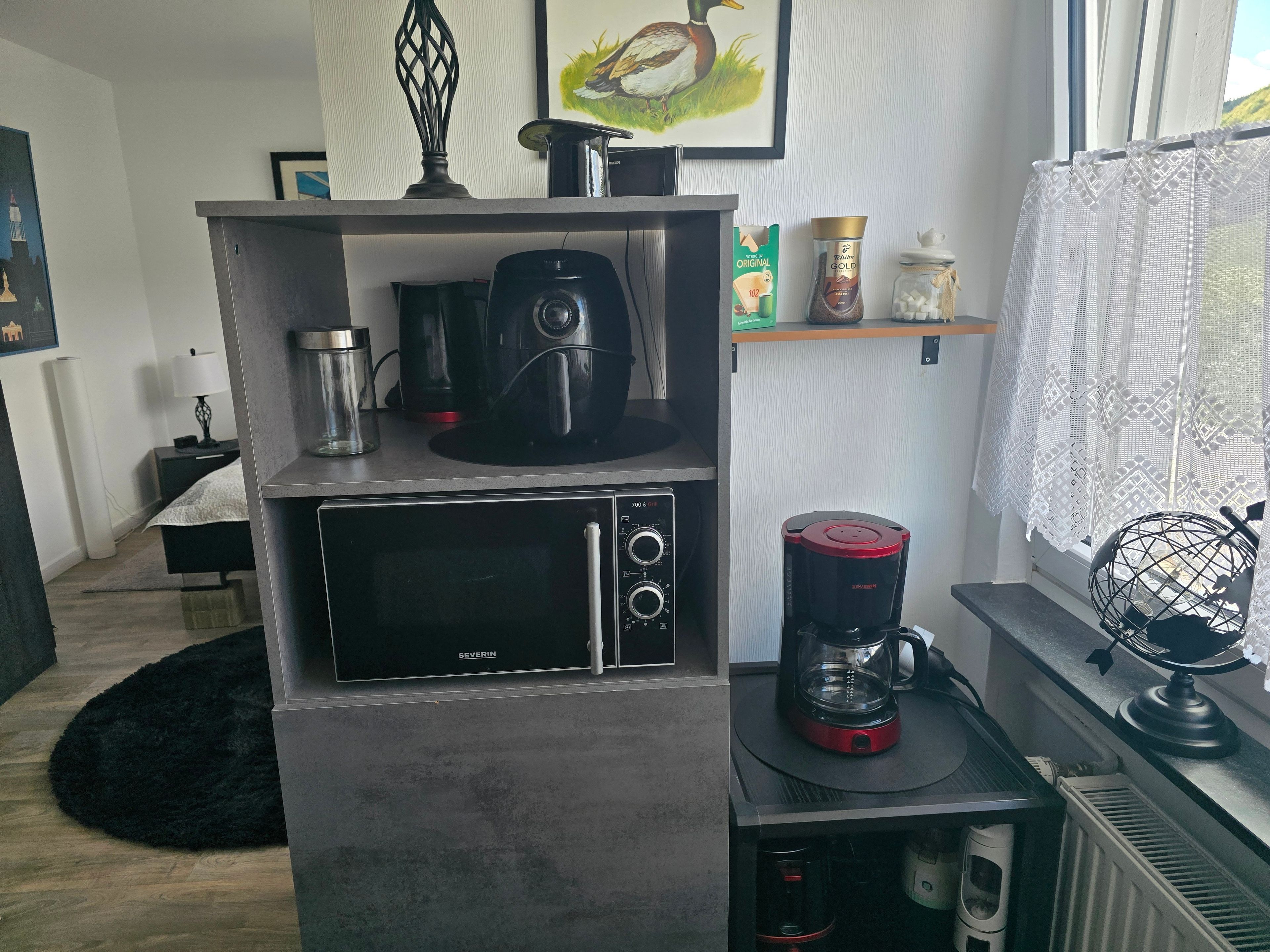 Una kitchenette equipada con microondas, cafetera y una alacena con utensilios de cocina.