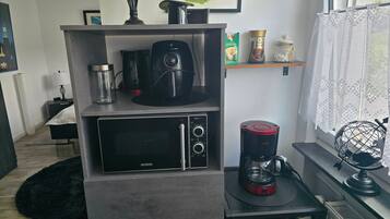 Una kitchenette equipada con microondas, cafetera y una alacena con utensilios de cocina.