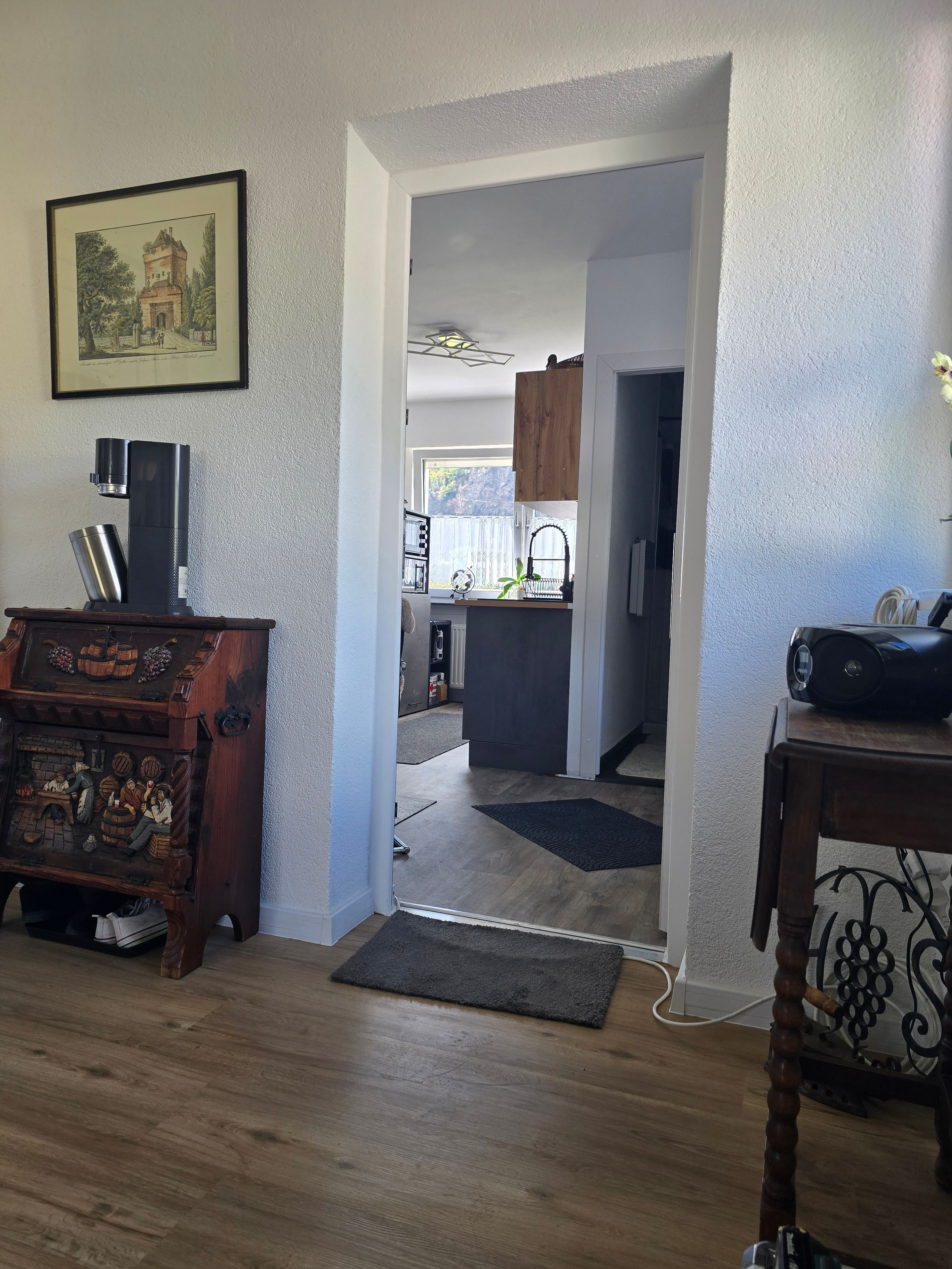 A room with a coffee maker, a wooden cabinet with a detailed carving, and a framed picture on the wall.
