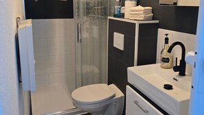 Un baño moderno con cabina de ducha de vidrio, inodoro, lavamanos con grifo negro y espejo sobre el lavamanos.