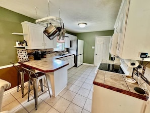 A kitchen with a central island, bar stools, a stove, and a refrigerator.