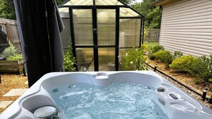 A hot tub with a clear view of the surrounding garden and a greenhouse structure. - Cozy Cabot 3 bedroom (Cabot)