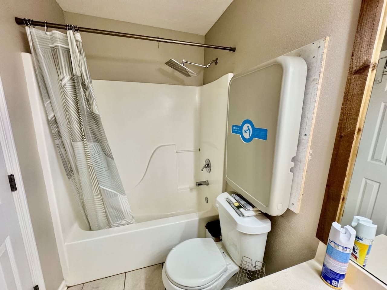 A bathroom with a shower, toilet, and a mirror with a hand sanitizer dispenser.