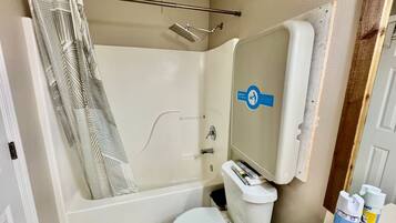 A bathroom with a shower, toilet, and a mirror with a hand sanitizer dispenser.