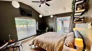 A bedroom with a large bed, a desk, a chair, a ceiling fan, and a window with blinds. - Cozy Cabot 3 bedroom (Cabot)