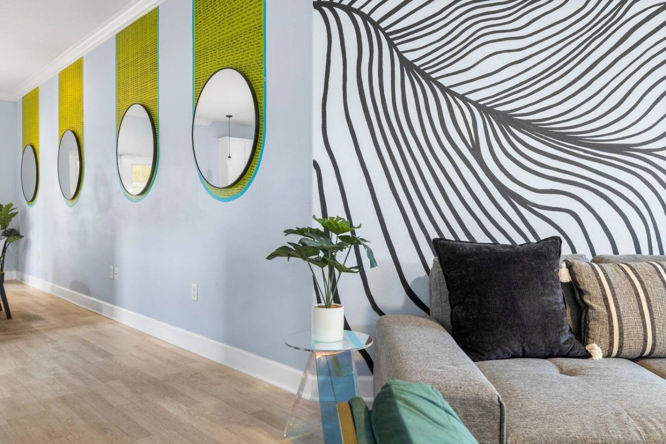 Un interior moderno con un sofá, una mesita con una planta y una pared con espejos circulares y un diseño abstracto grande.