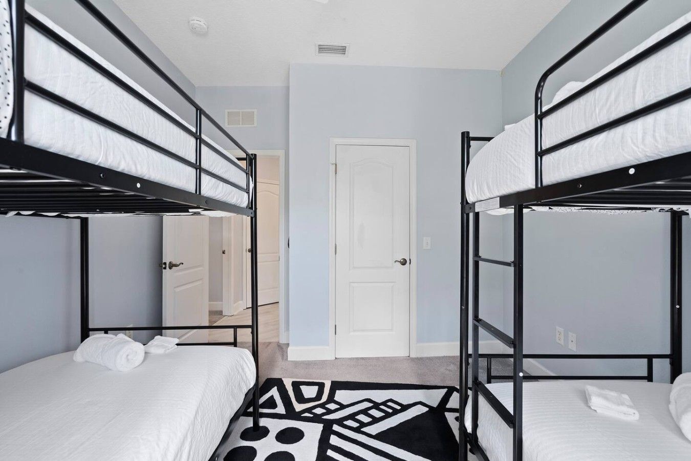 A room with bunk beds, a patterned rug, and a white door.