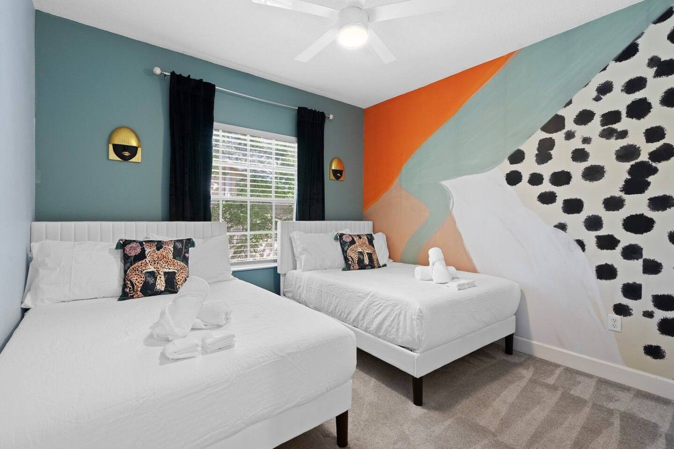 A hotel room with two beds, a large window with curtains, a ceiling fan, and a wall with a geometric pattern.