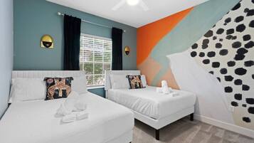 A hotel room with two beds, a large window with curtains, a ceiling fan, and a wall with a geometric pattern.