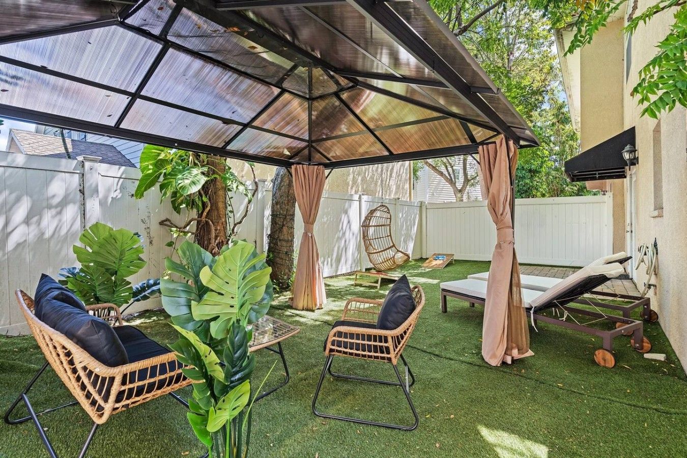 A covered outdoor seating area with artificial grass, wicker furniture, and a pergola structure.