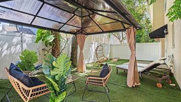 A covered outdoor seating area with artificial grass, wicker furniture, and a pergola structure.
