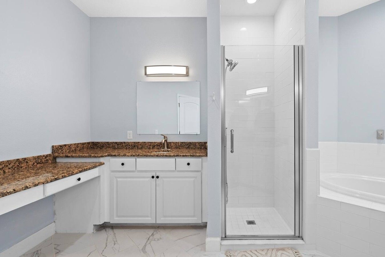A modern bathroom with a granite countertop, a glass shower enclosure, and a white bathtub.