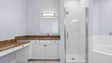 A modern bathroom with a granite countertop, a glass shower enclosure, and a white bathtub.