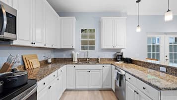 Una cocina moderna con armarios blancos, encimeras de granito, horno empotrado y microondas.