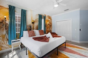 Une chambre à coucher avec un lit, des rideaux, une fresque murale, un ventilateur de plafond et une porte.