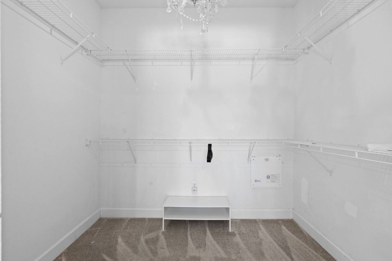A room with a white floor, a white bench, and a chandelier.