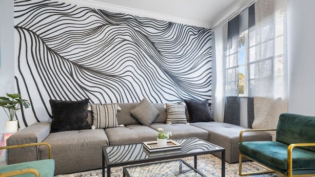 Uma sala de estar moderna com um sofá, duas poltronas, uma mesa de centro e um tapete estampado.