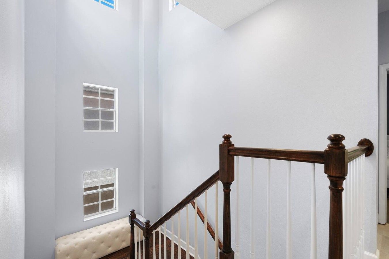 A staircase with a wooden handrail and white balusters, leading to a landing with a cushioned bench.