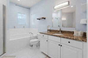 Une salle de bain moderne équipée d’une baignoire, de toilettes, d’un meuble-lavabo et d’un grand miroir.