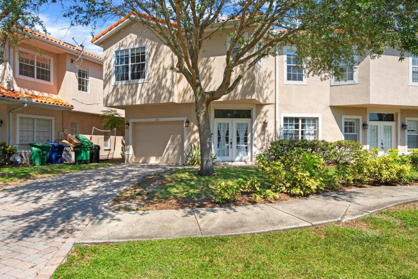 A two-story residential building with a garage, a tree in the front yard, and a well-maintained lawn.